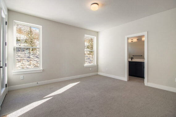 Empty room with carpet, two windows, and bathroom doorway