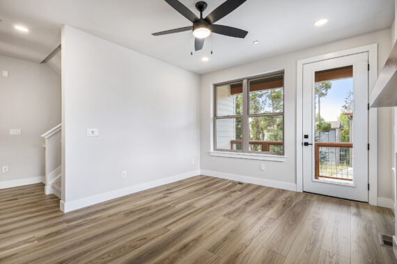 Empty room with wooden floors, ceiling fan, window, and door