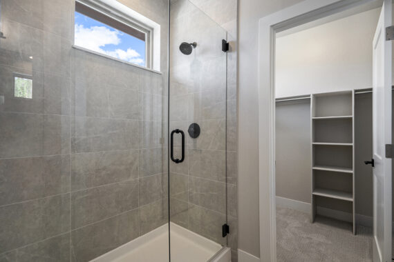 Glass shower with gray tiles next to a walk-in closet