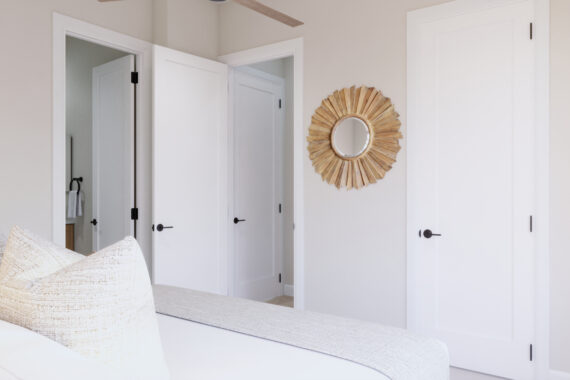 A bedroom with white doors and sunburst mirror